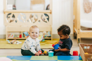 Two infant children sitting on a mat in classroom