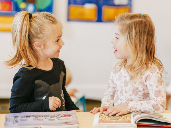 Two preschoolers smiling at one another in classroom