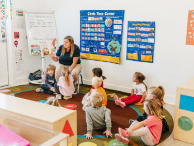 Teacher in classroom setting teaching children sitting on floor